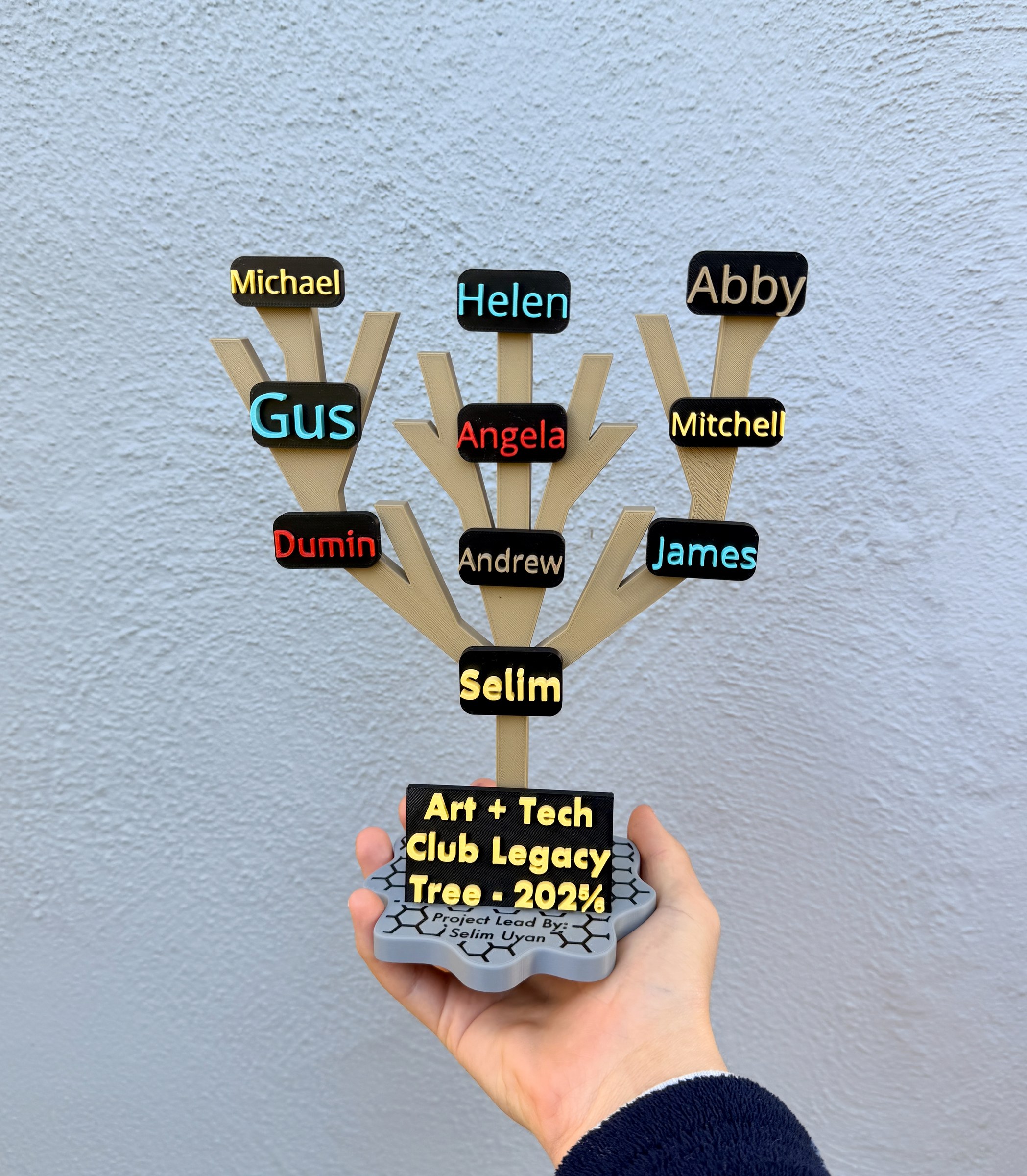 A hand holds the Art + Tech Club Legacy Tree, with members’ names branching from its base.